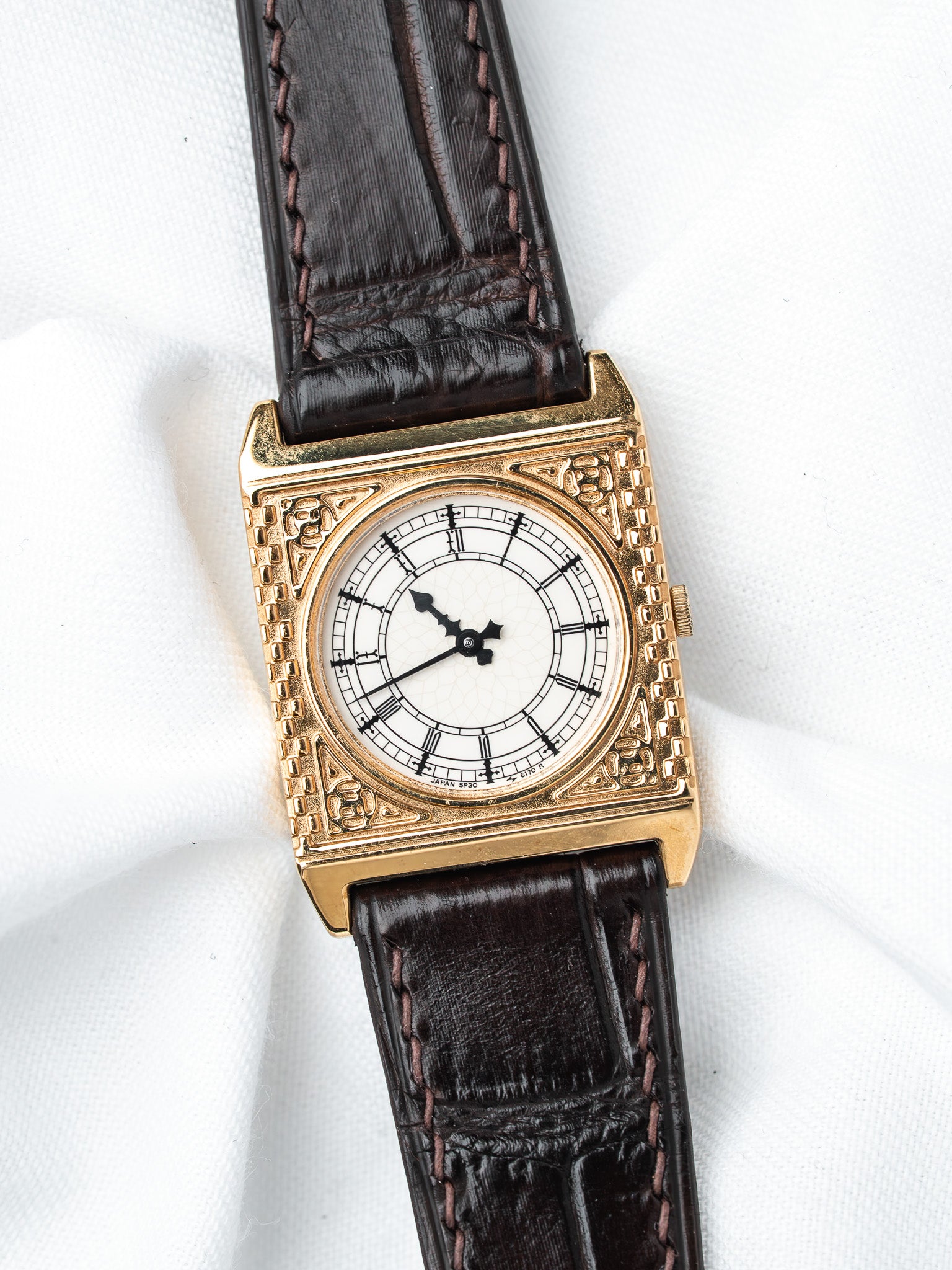 Vintage gold watch with white dial, black hands, and brown leather strap