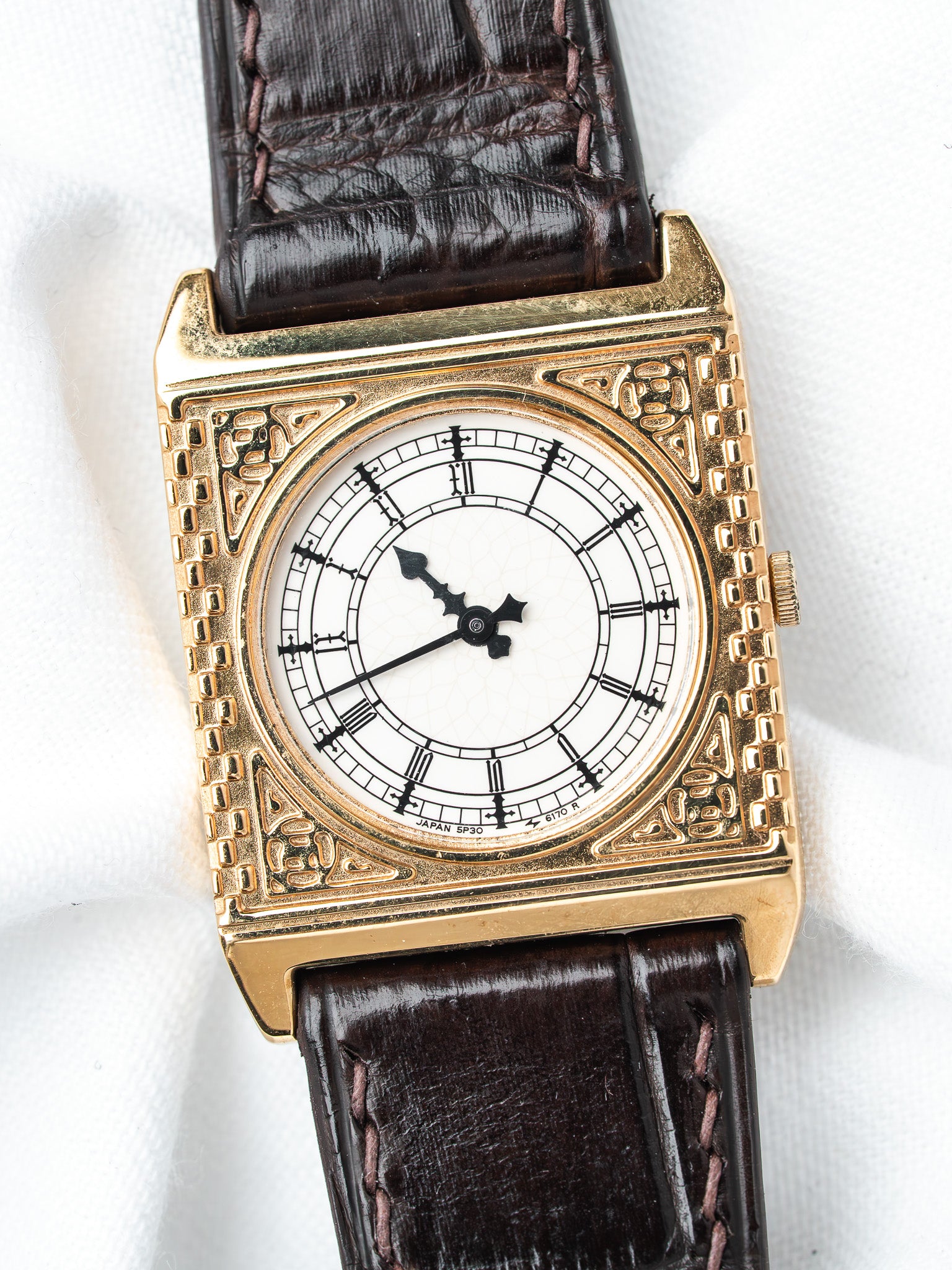 Vintage rectangular gold watch with white dial, Roman numerals, and brown leather strap