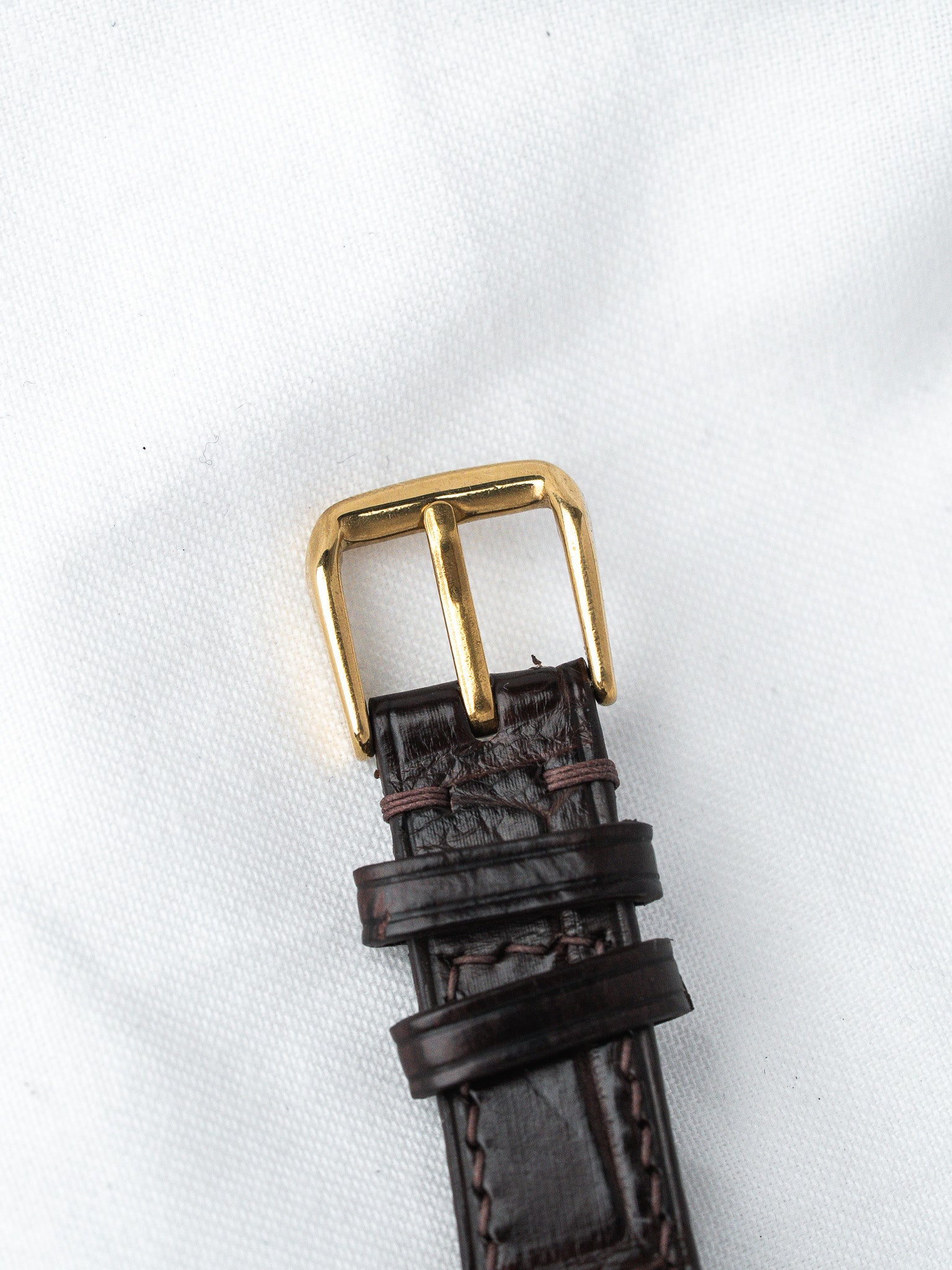 Brown leather watch strap with gold buckle and visible stitching on white background