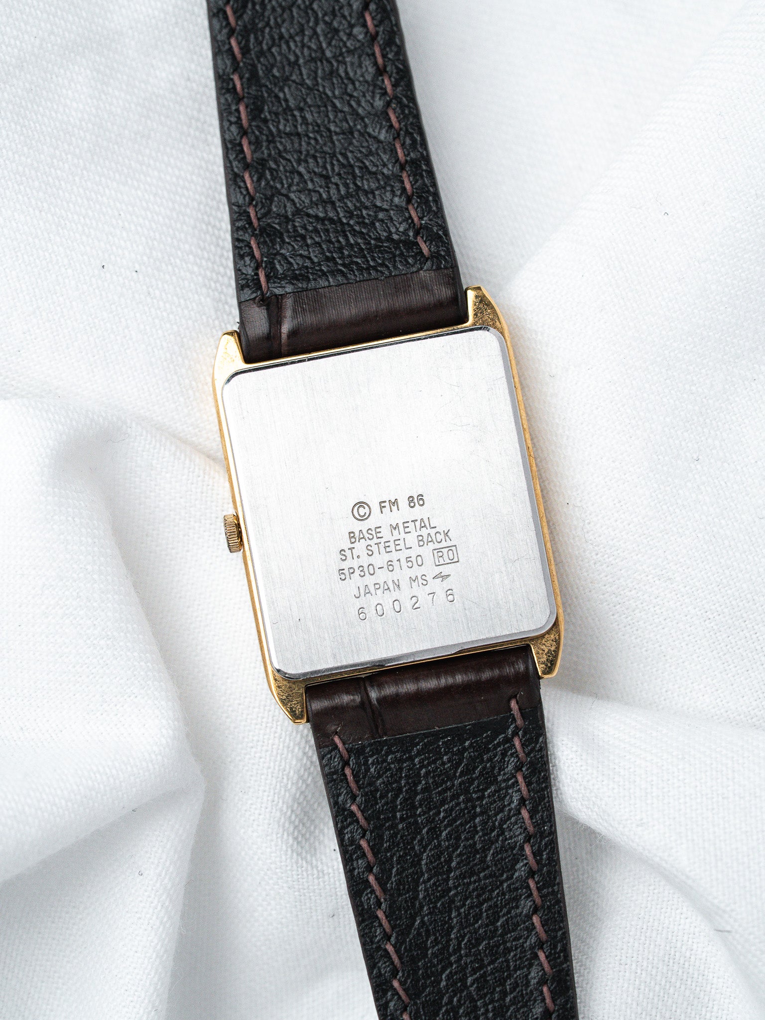 Vintage watch with gold case, black leather strap, and engraved steel back