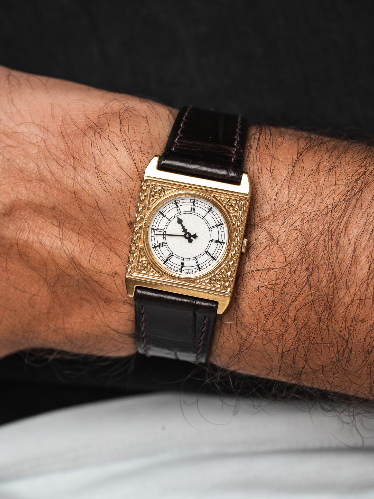 Vintage square gold watch with white dial, brown leather strap worn on wrist