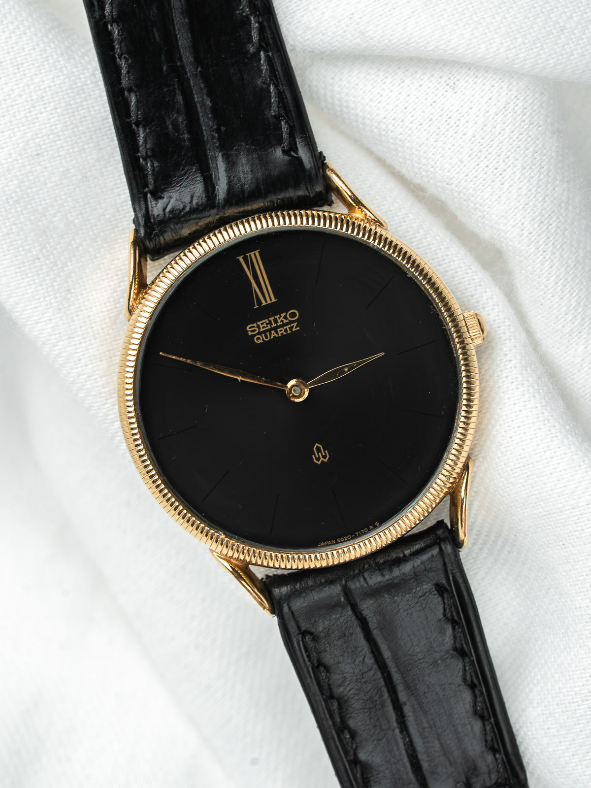 Montre Seiko Quartz vintage, boîtier doré, cadran noir et bracelet en cuir noir