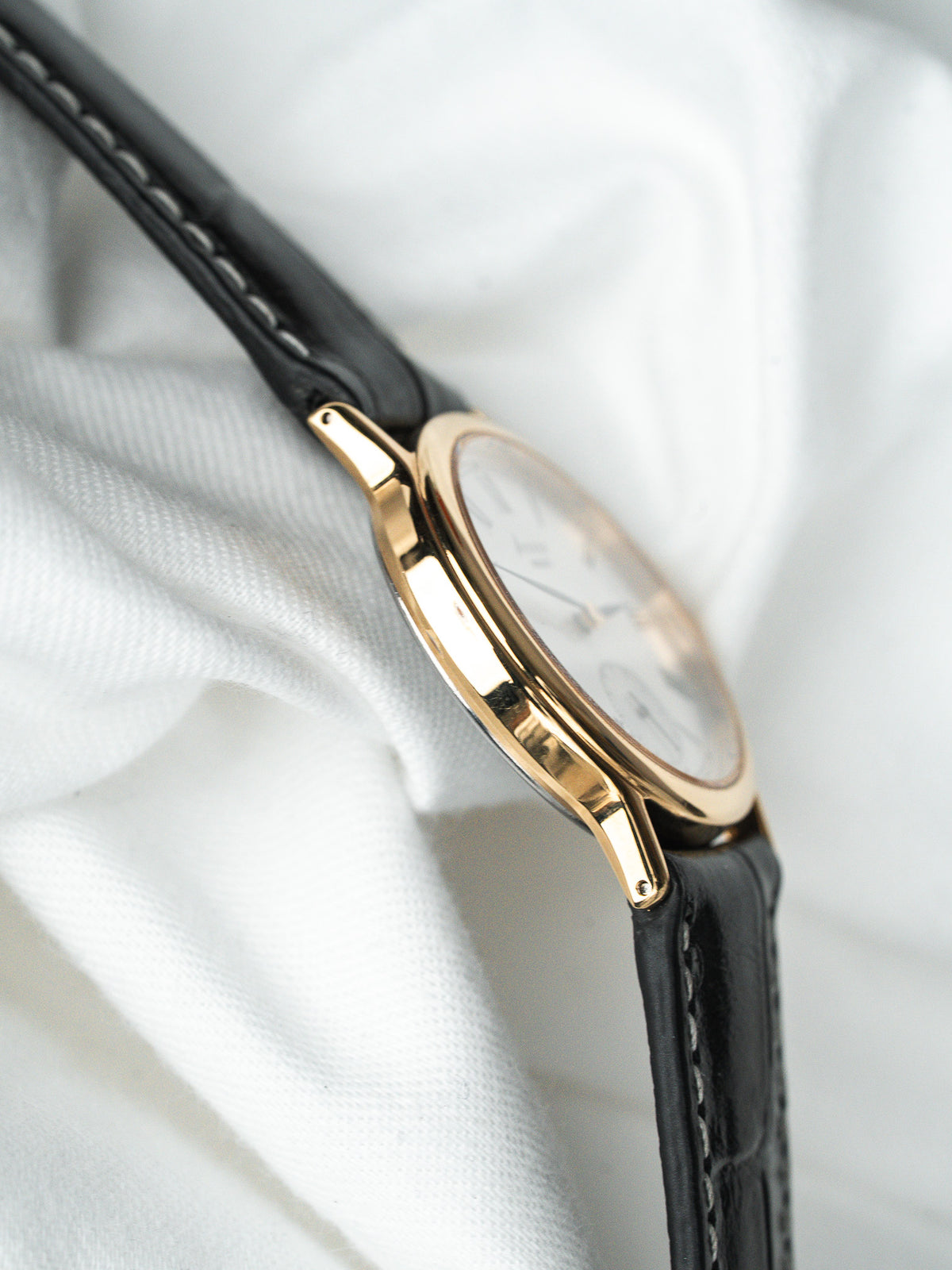 Montre vintage boîtier or, cadran blanc et bracelet en cuir noir sur tissu blanc