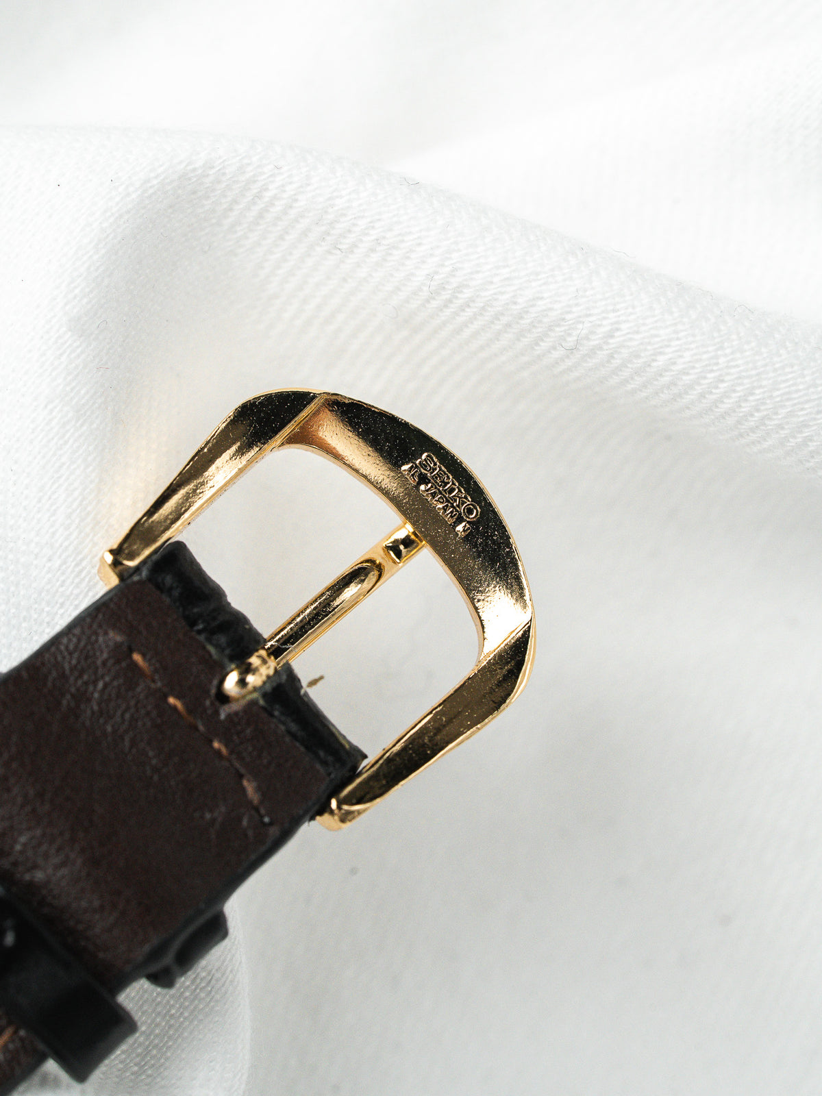 Boucle de bracelet Seiko dorée sur cuir marron, posée sur un fond blanc