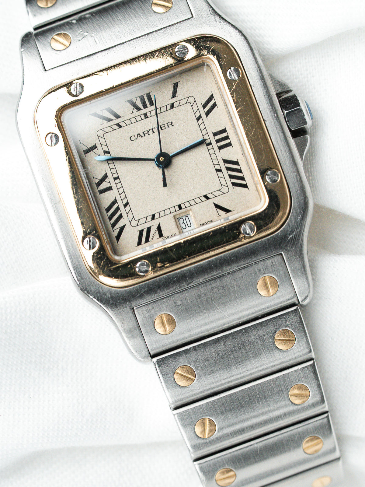 Montre Cartier vintage en acier, boîtier rectangulaire et cadran blanc sur fond textile