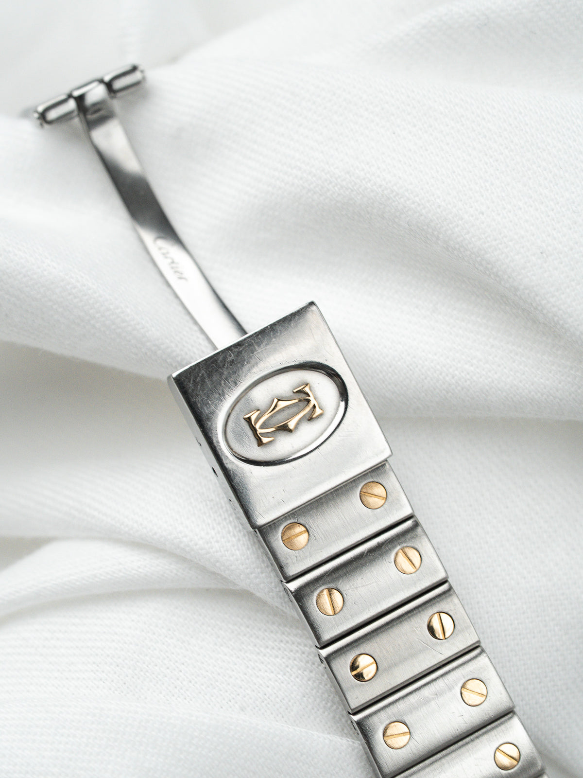 Bracelet de montre Cartier en acier avec détails dorés sur fond de tissu blanc