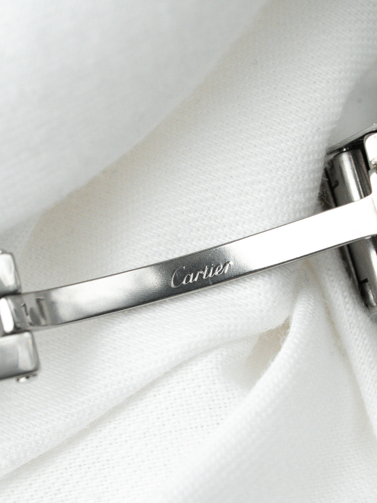 Détail du fermoir d'un bracelet de montre Cartier en acier sur fond blanc