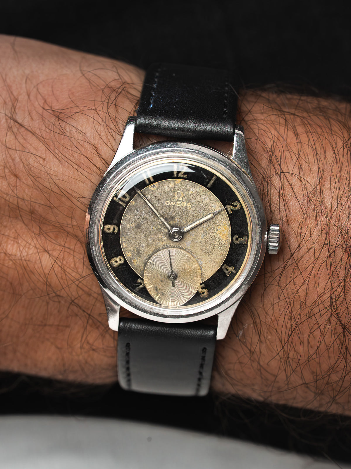 Montre Omega vintage à cadran patiné et bracelet en cuir noir, portée au poignet