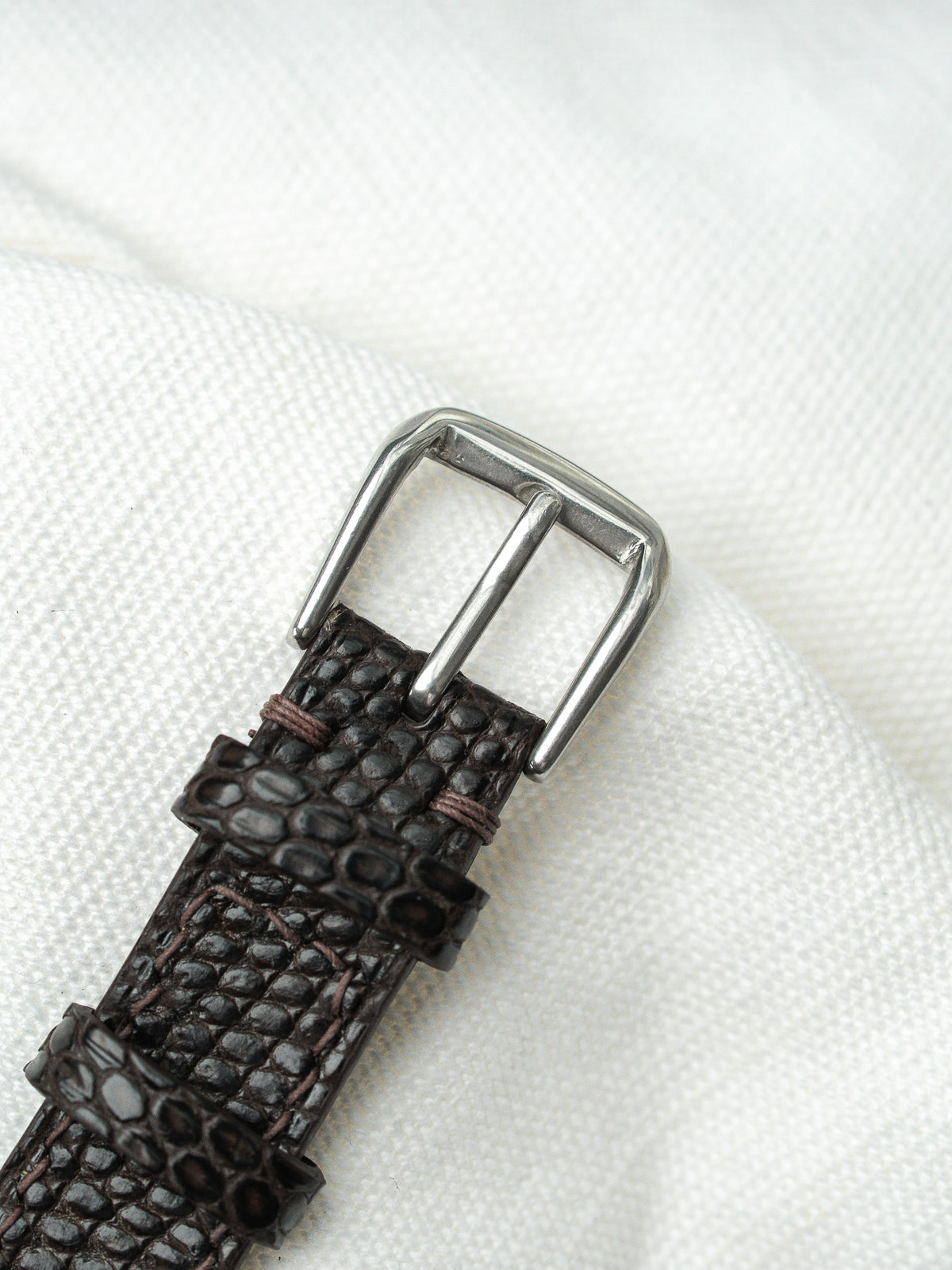 Gros plan d'un bracelet de montre en cuir noir texturé avec boucle argentée.