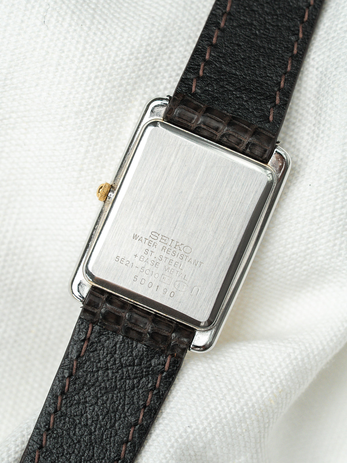 Dos d'une montre Seiko rectangulaire en acier avec bracelet en cuir noir.
