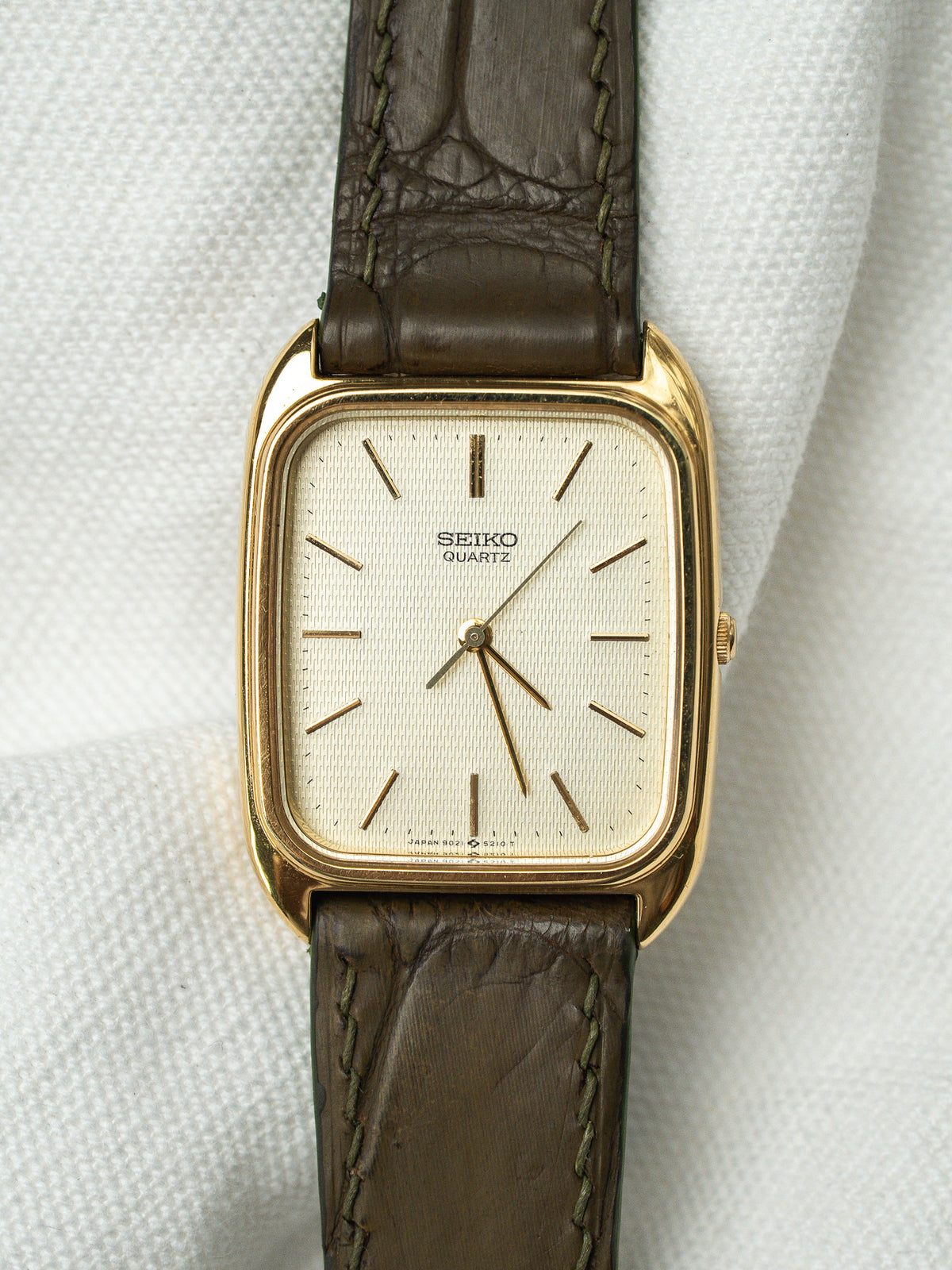 Montre Seiko Quartz vintage au boîtier doré rectangulaire et bracelet en cuir marron.