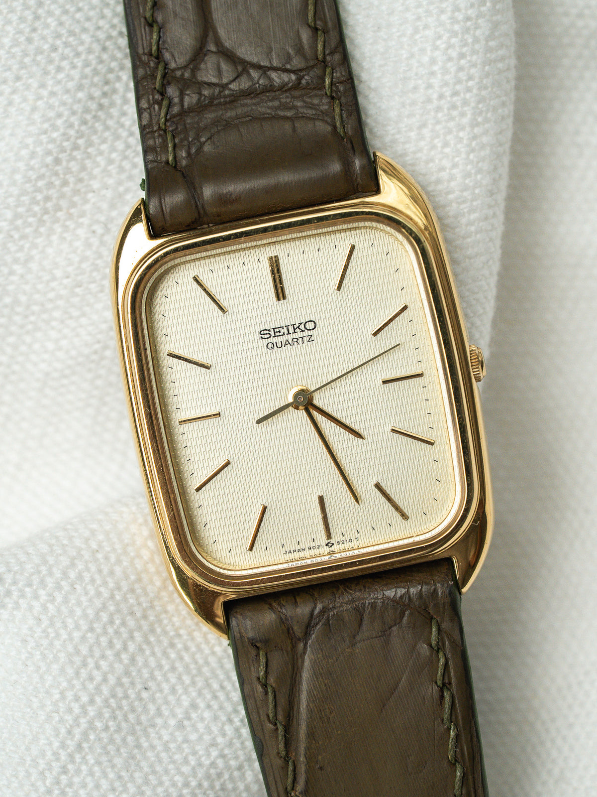Montre Seiko Quartz vintage avec boîtier doré rectangulaire et bracelet en cuir marron.