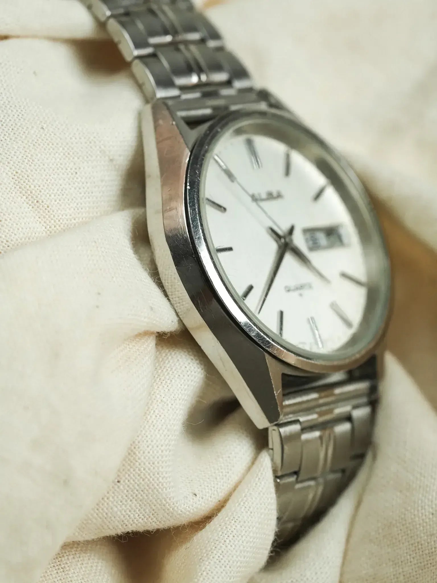 Alba vintage watch with white dial, steel bracelet, resting on cream fabric