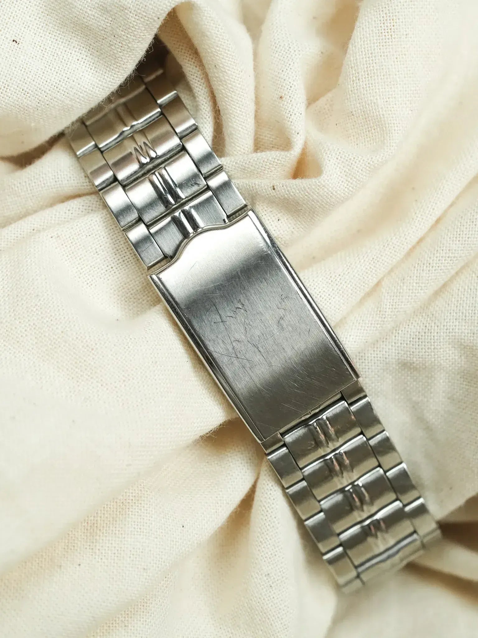 Vintage Omega steel bracelet with brushed clasp, resting on cream fabric