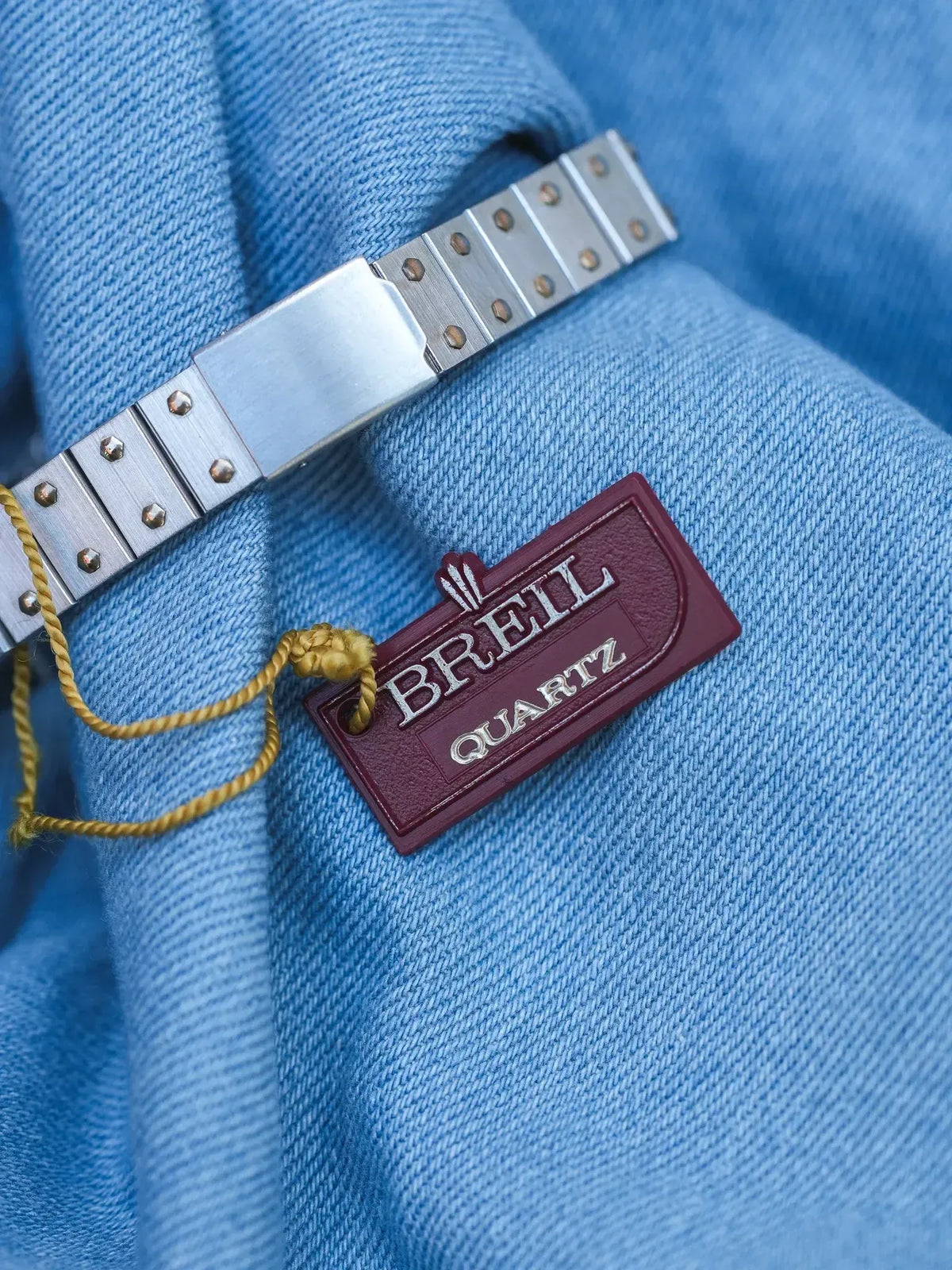Breil Quartz watch bracelet in brushed steel with maroon tag on blue fabric