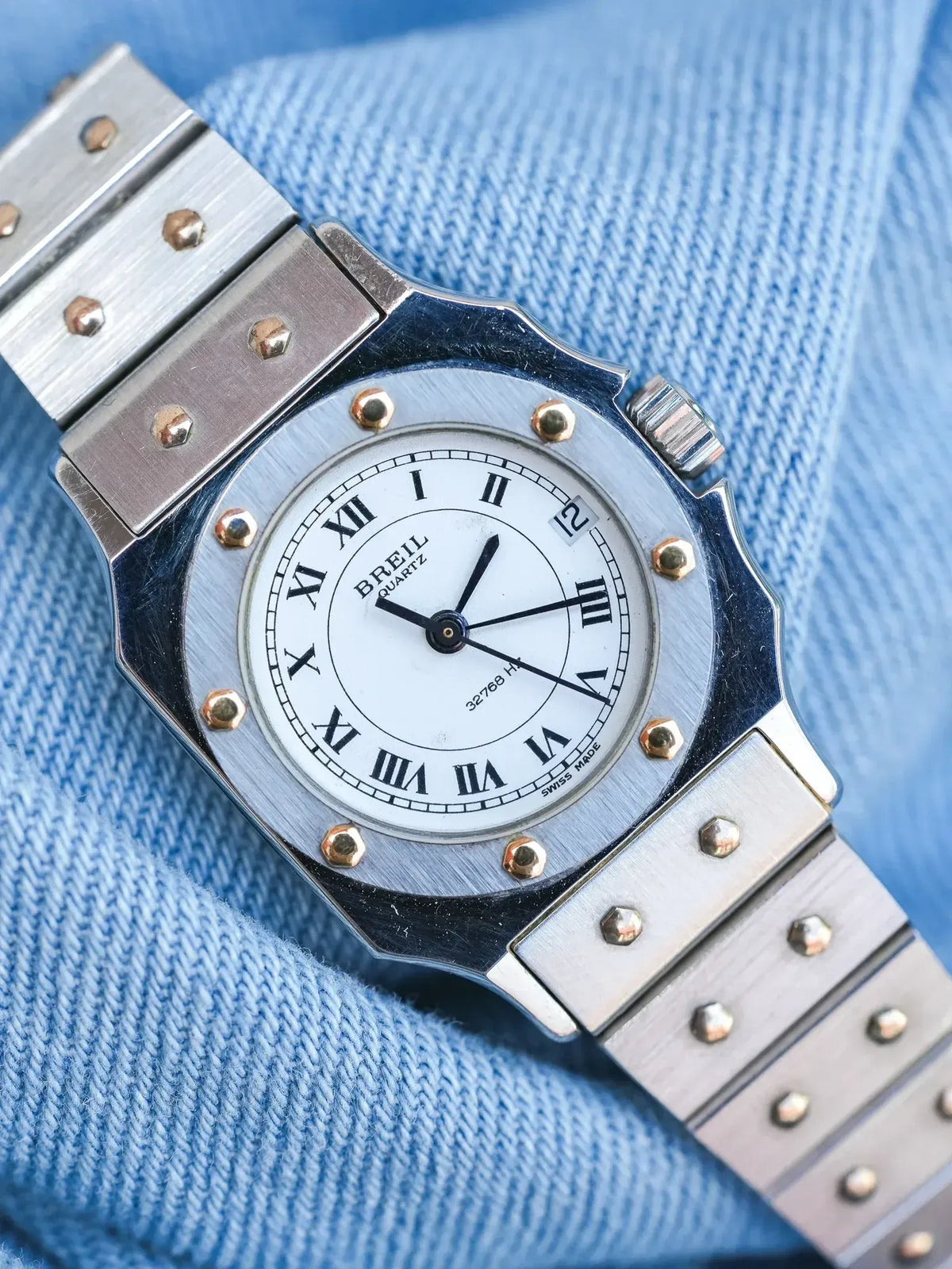 Breil quartz watch with white dial, Roman numerals, and steel bracelet on blue fabric