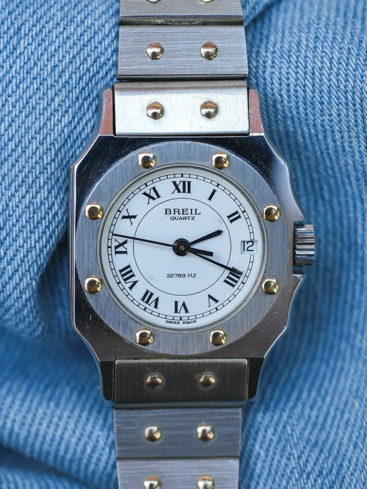 Breil Quartz vintage watch with white dial, Roman numerals, and steel bracelet on denim