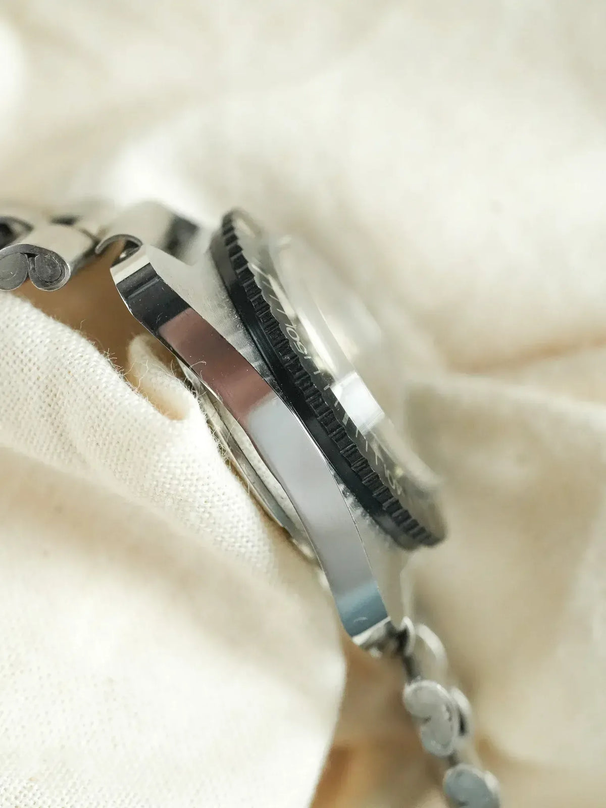 Vintage Rolex Submariner side view, stainless steel case, black bezel, on white fabric