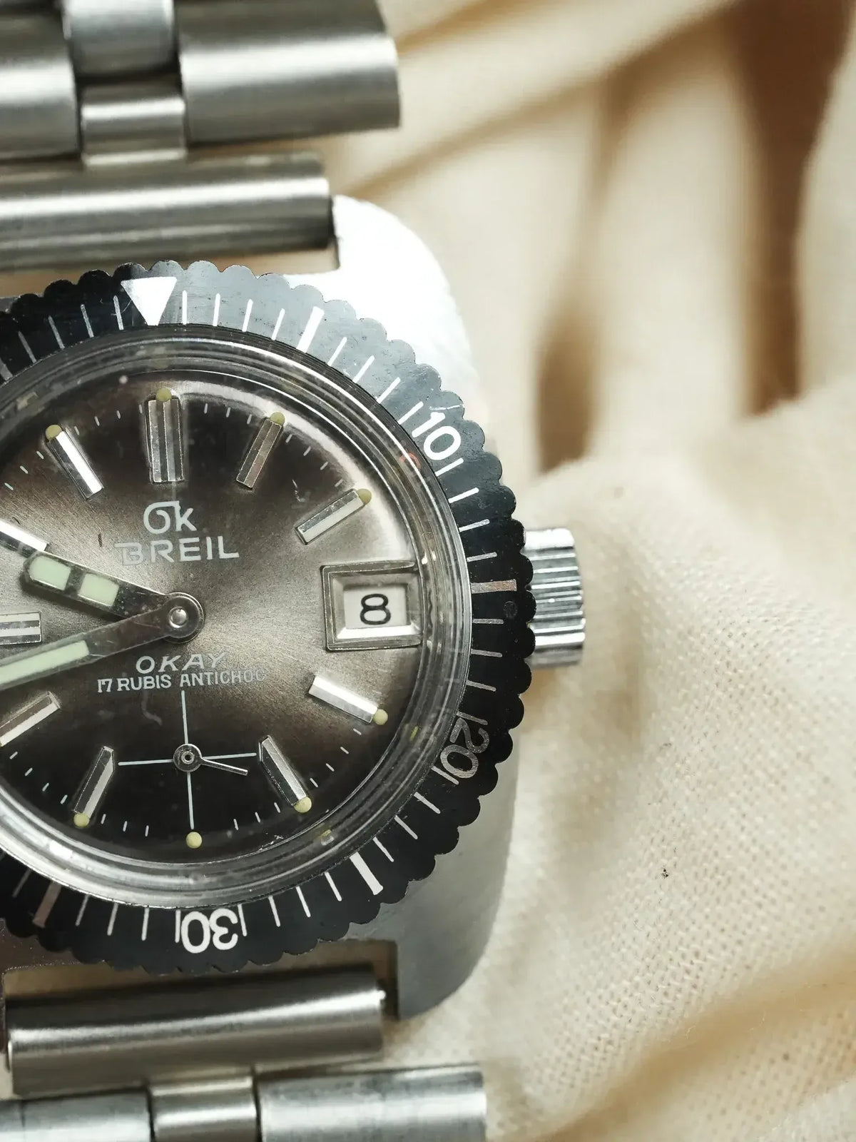 Vintage OKAY Breil diver watch with black dial, steel bracelet, and rotating bezel