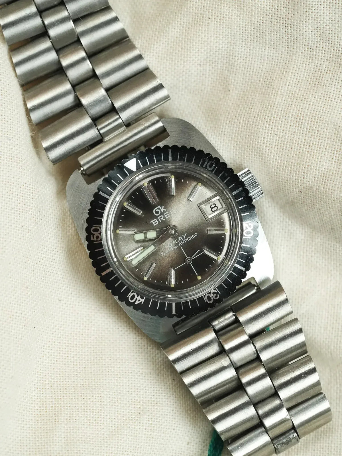 Vintage Breil OKAY diver watch with black dial, steel bracelet, and rotating bezel