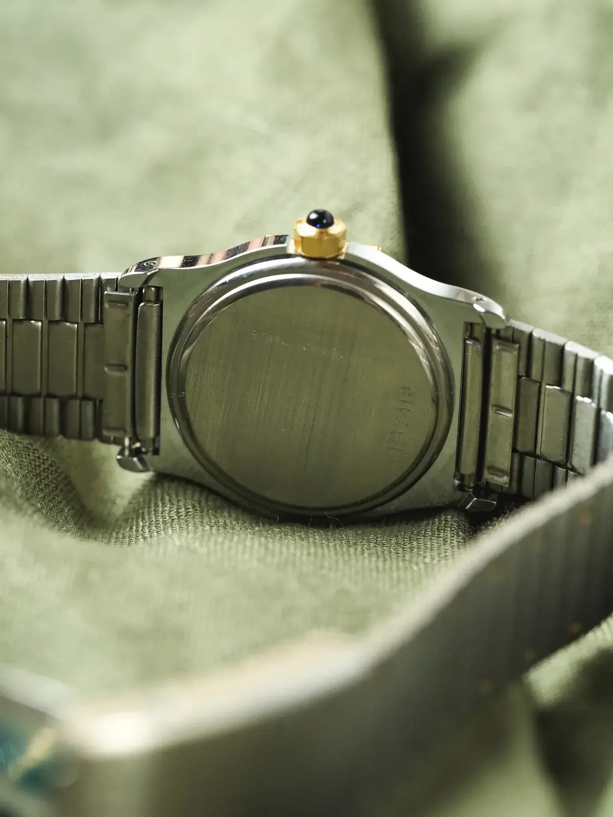 Cartier watch back view, stainless steel case, gold crown with blue cabochon, on green fabric