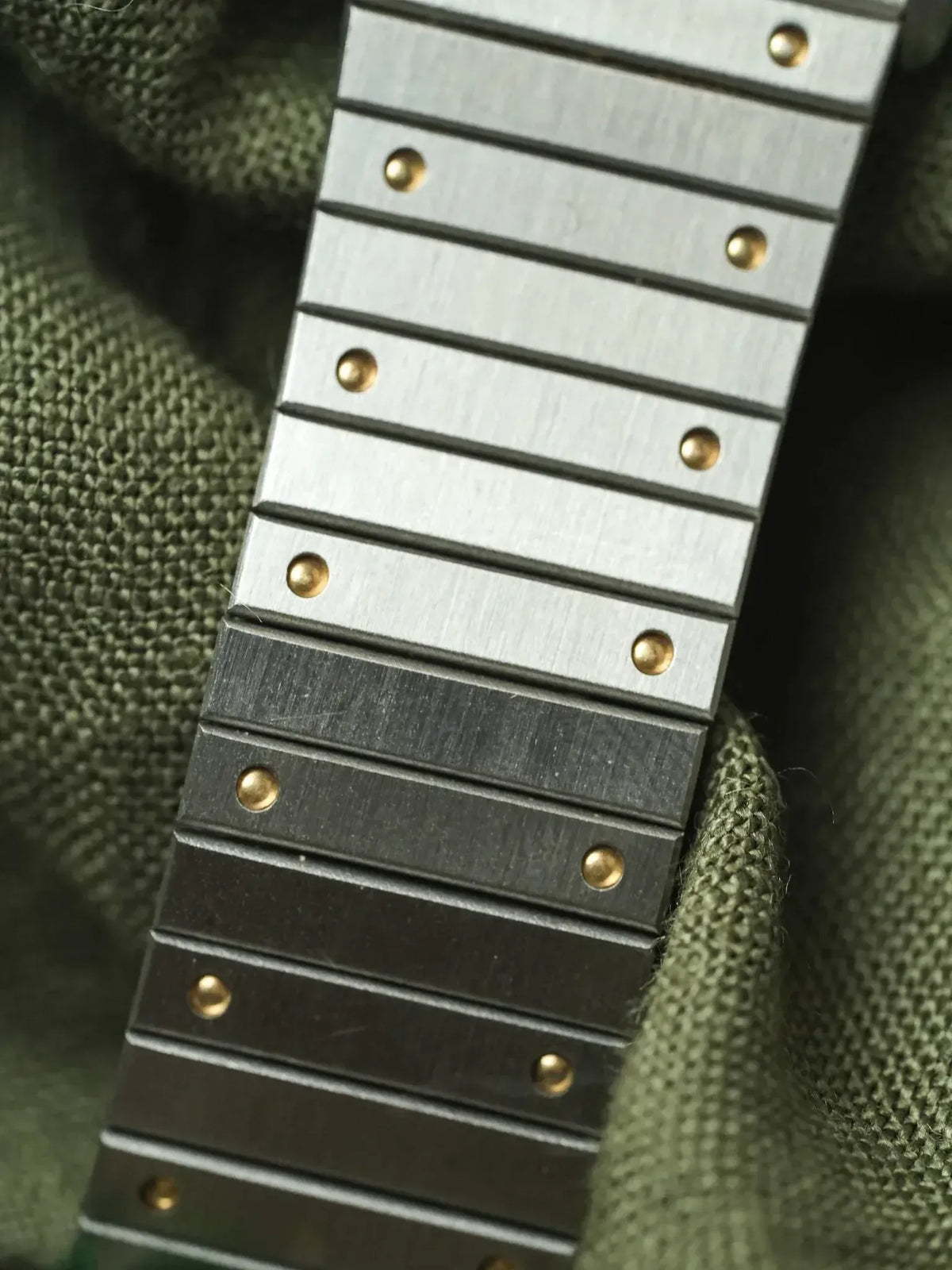 Vintage Rolex Oyster bracelet with brushed steel links and gold pins on green fabric