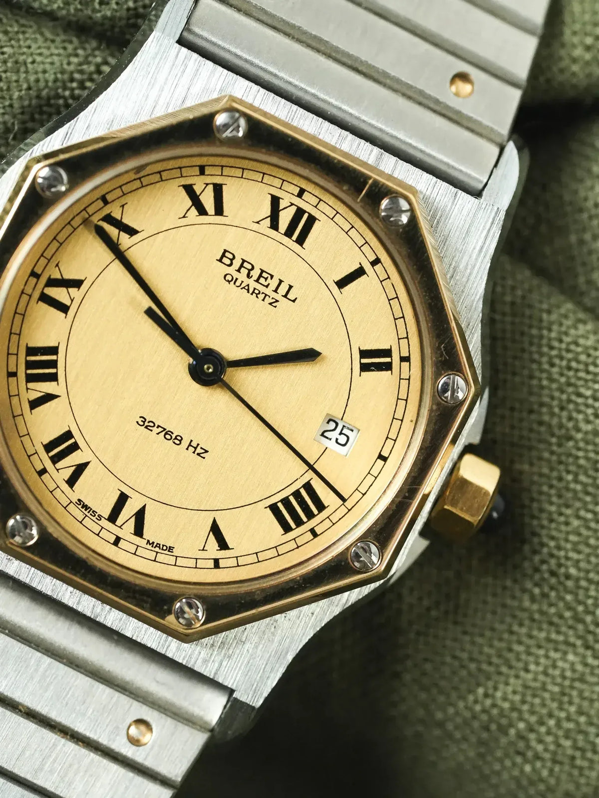 Breil quartz watch with gold dial, Roman numerals, and stainless steel bracelet on textured fabric