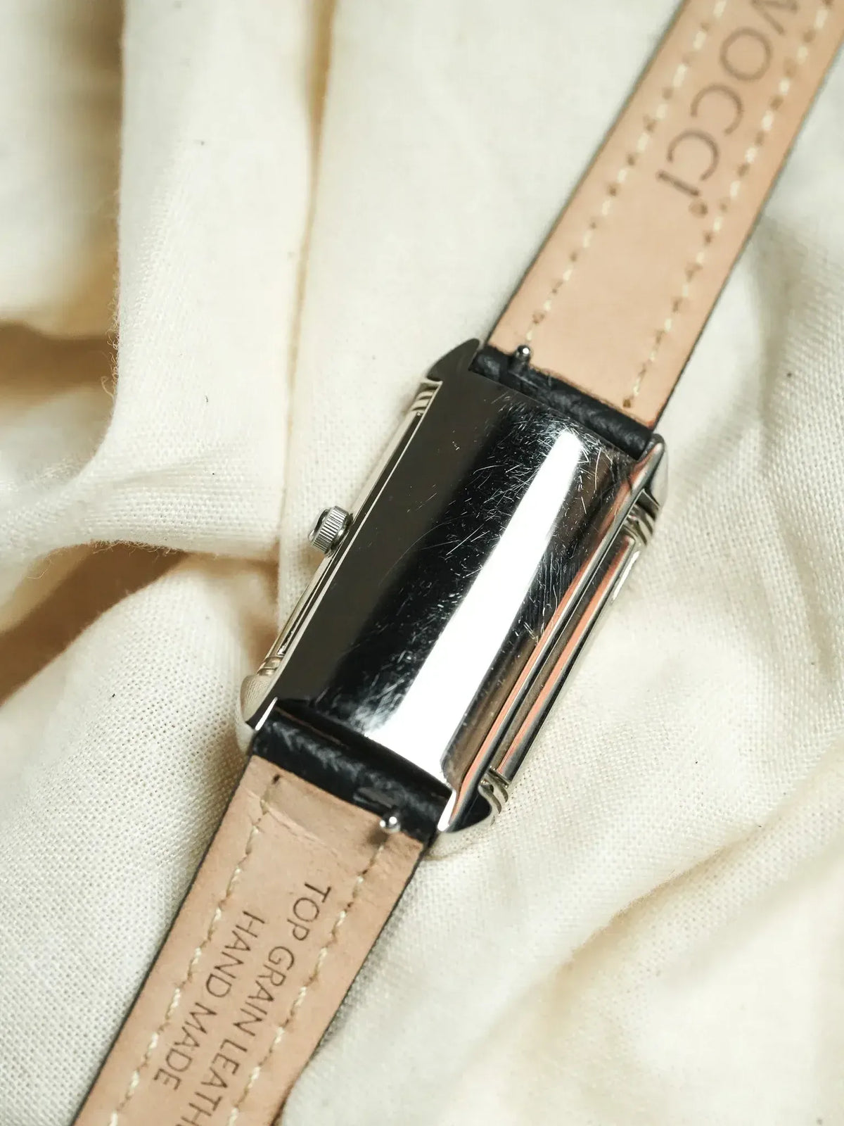 Vintage rectangular watch with silver case and tan leather strap on fabric
