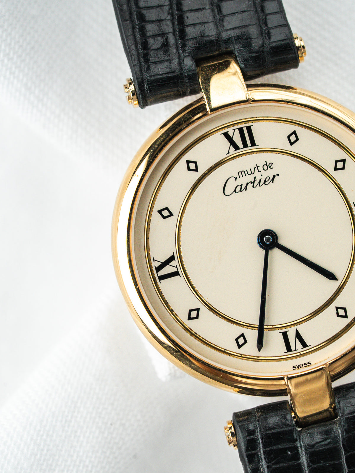 Montre Cartier Must vintage, boîtier rond doré, cadran blanc et bracelet cuir noir