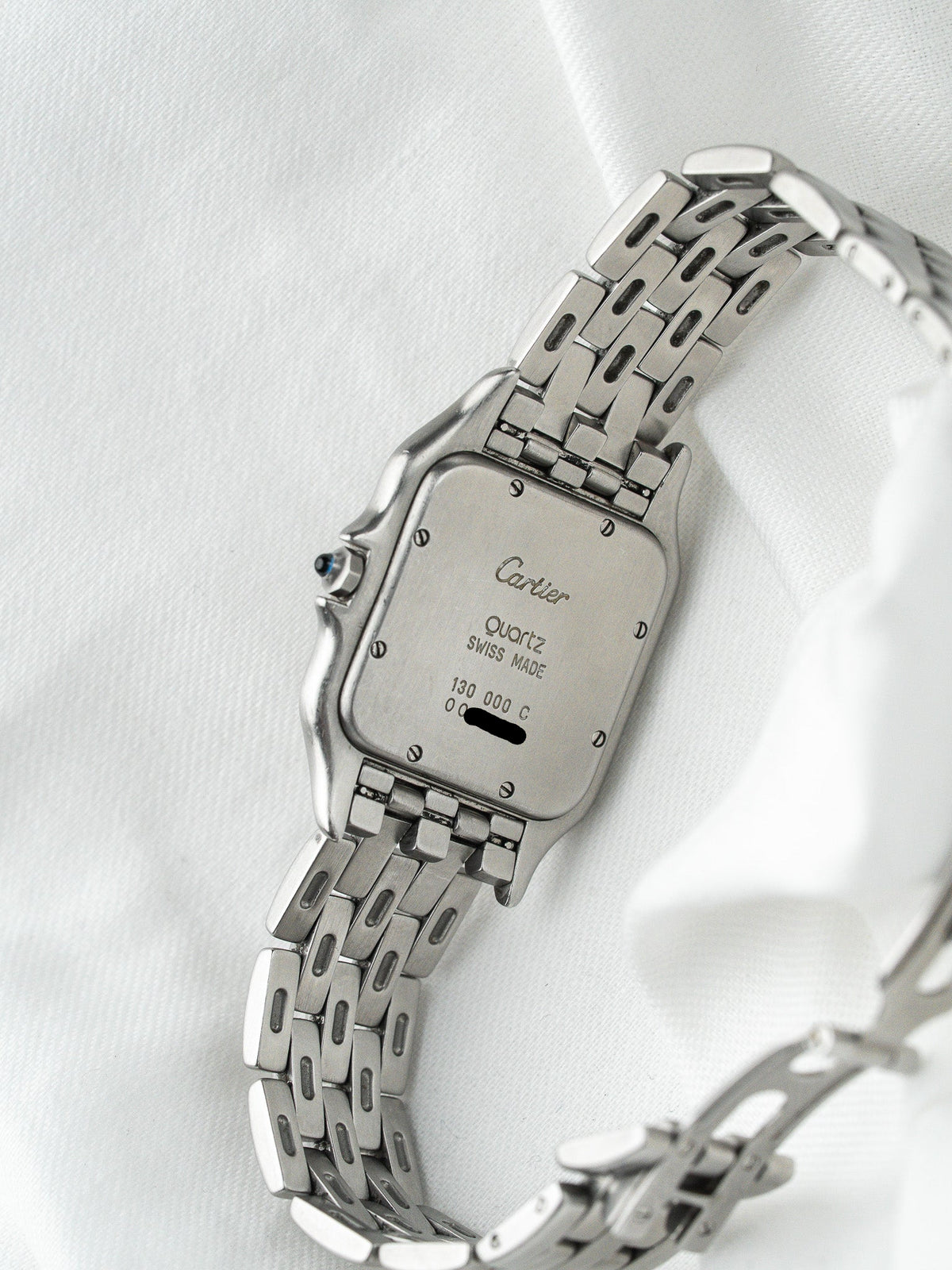 Dos d'une montre Cartier vintage en acier avec bracelet à mailles sur fond blanc