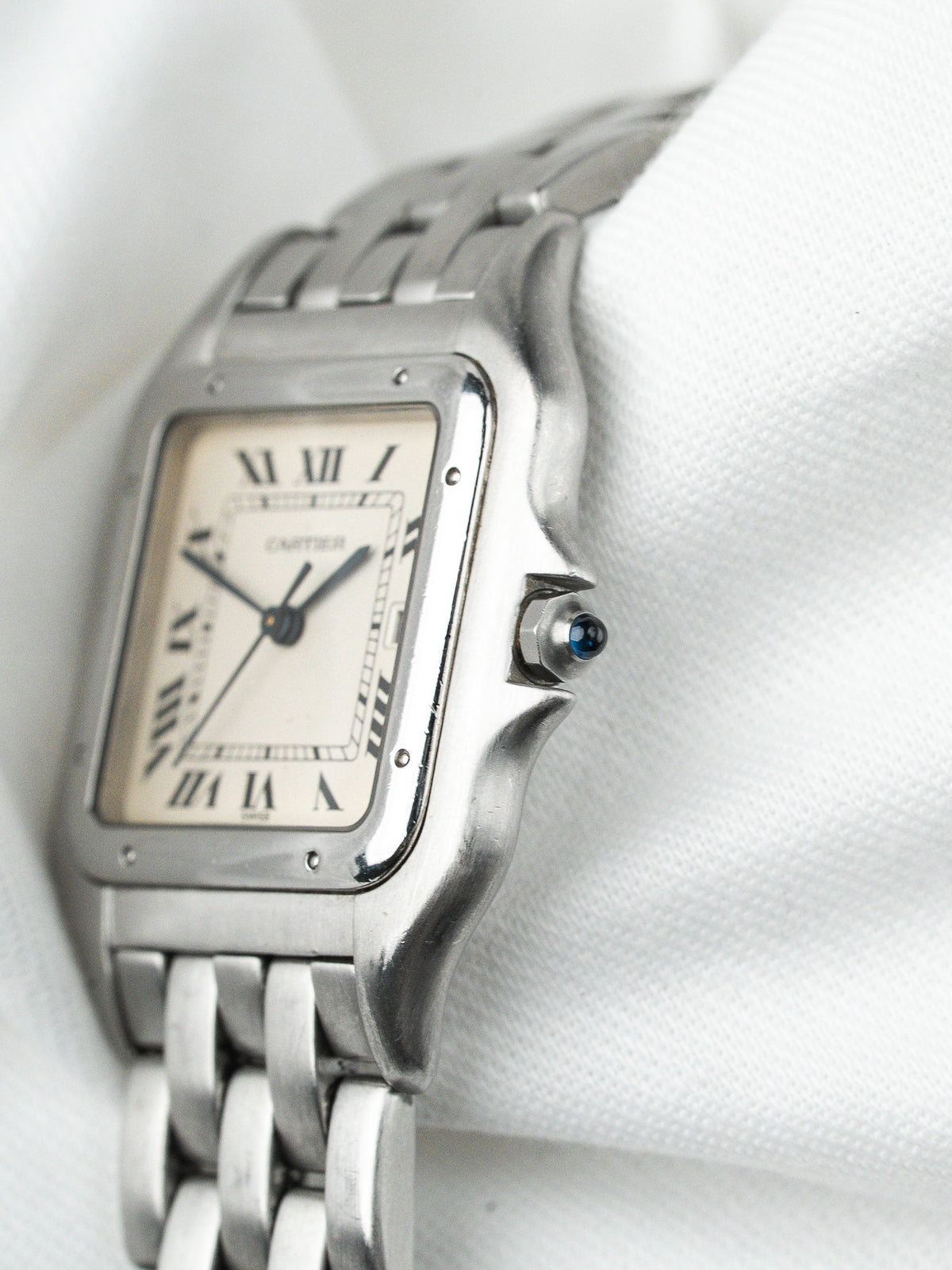 Montre Cartier vintage en acier, boîtier rectangulaire et cadran blanc sur fond textile