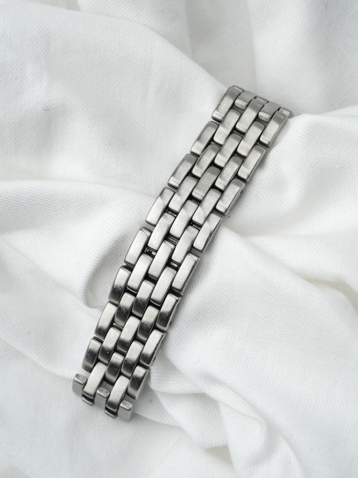Bracelet de montre en acier inoxydable argenté posé sur un tissu blanc froissé