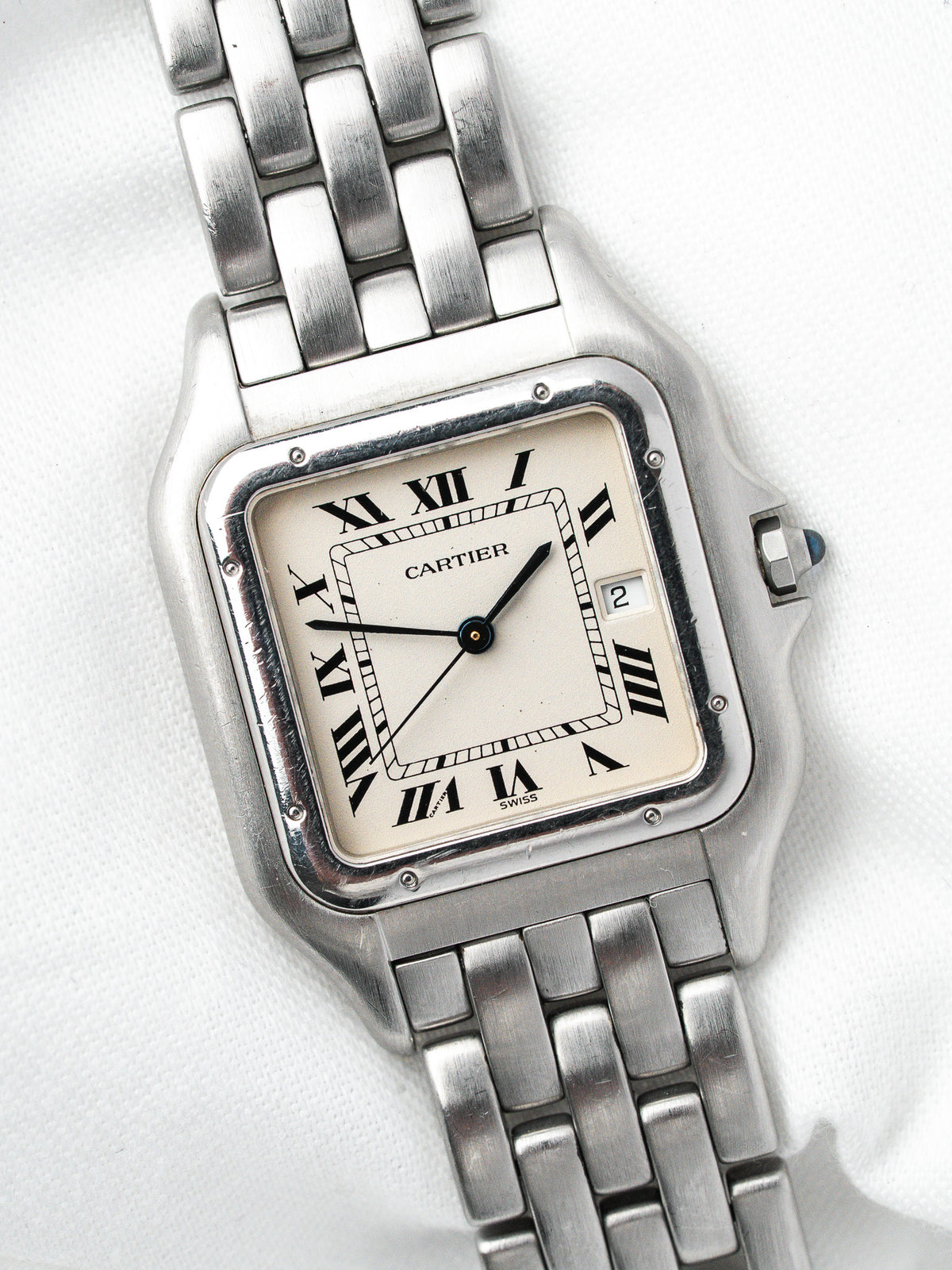 Montre Cartier vintage en acier, boîtier rectangulaire et cadran blanc sur fond neutre