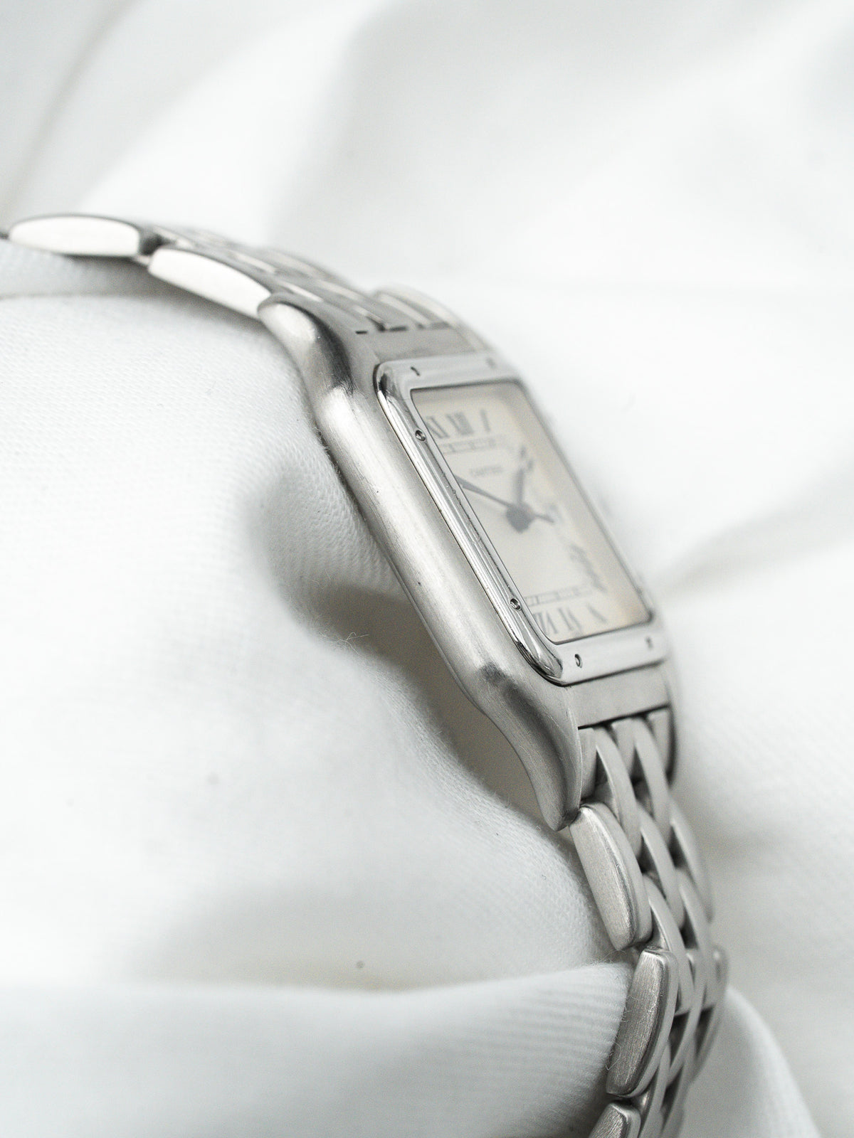 Montre Cartier vintage en acier avec boîtier rectangulaire et bracelet à mailles, fond blanc