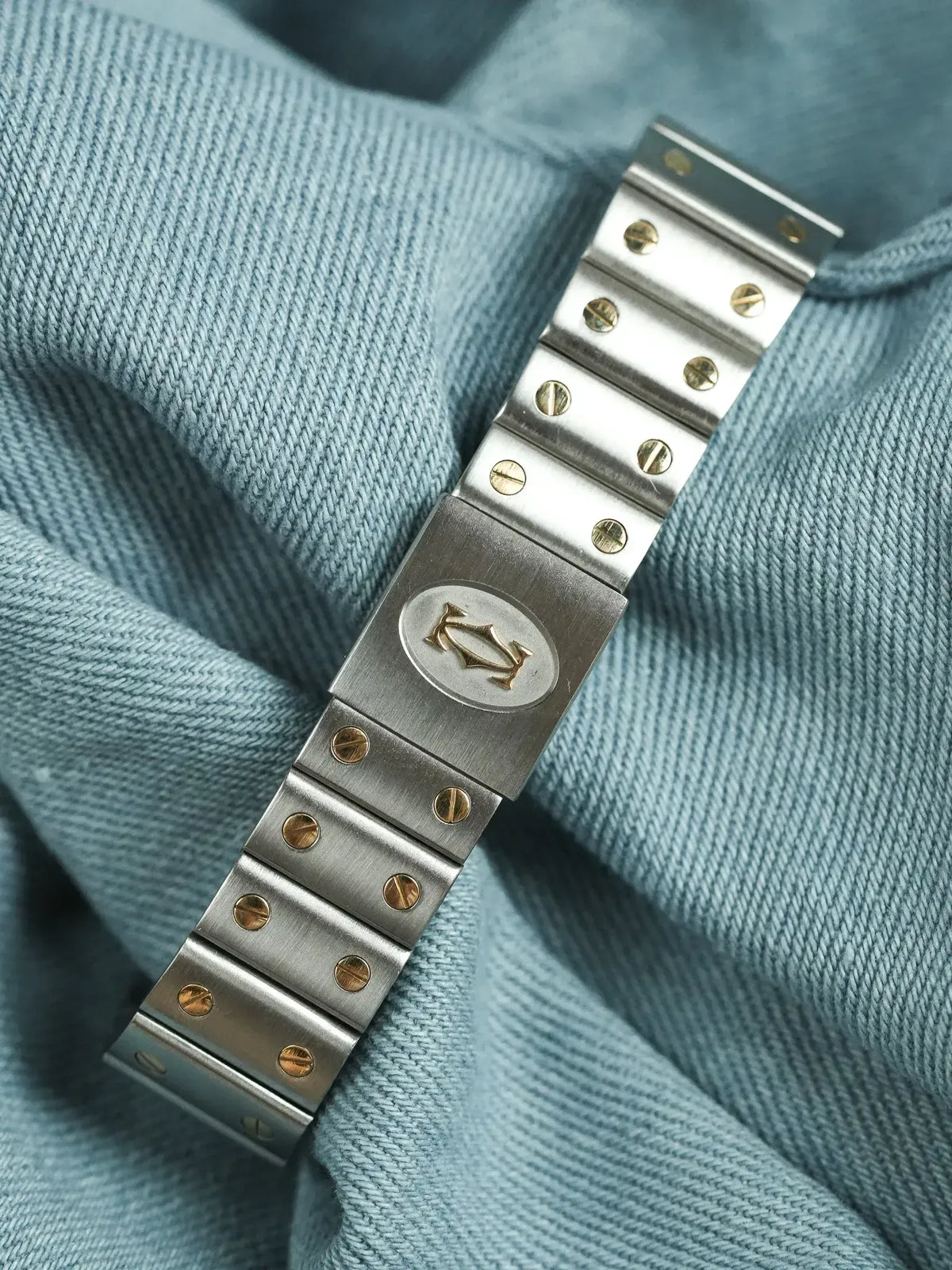 Cartier vintage bracelet with gold screws and logo, resting on blue fabric