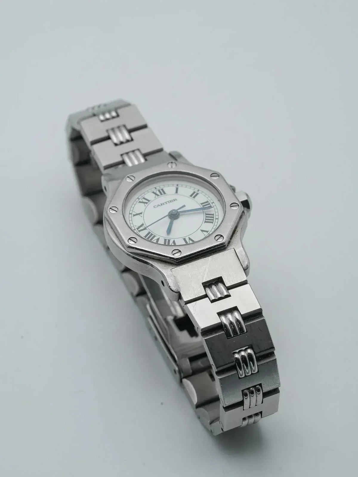Cartier Santos watch with octagonal case, white dial, Roman numerals, steel bracelet on neutral background