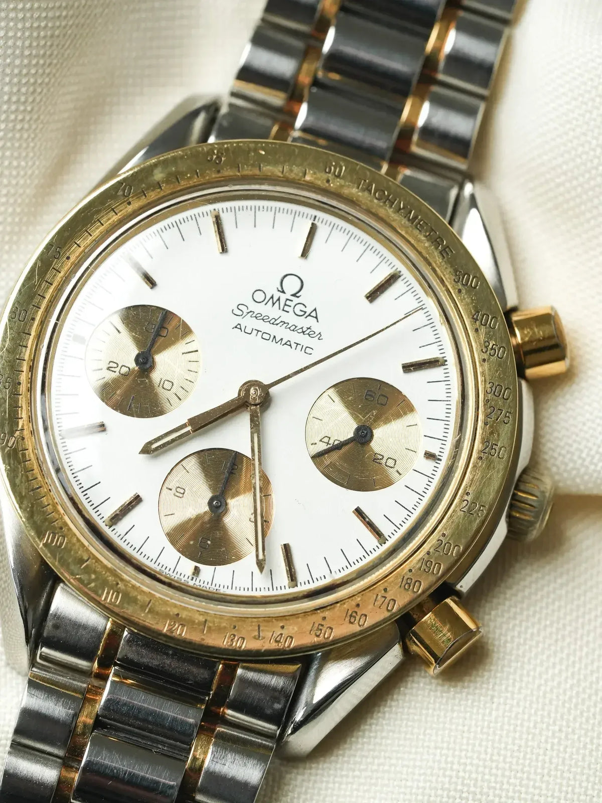 Vintage Omega Speedmaster Automatic chronograph with white dial, gold subdials, and two-tone bracelet