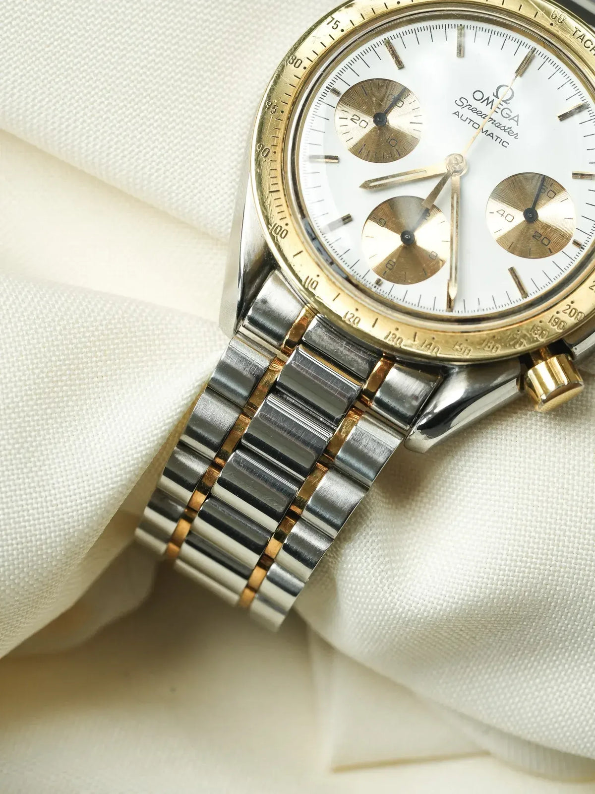 Omega Speedmaster vintage chronograph with white dial, gold accents, and two-tone bracelet on fabric