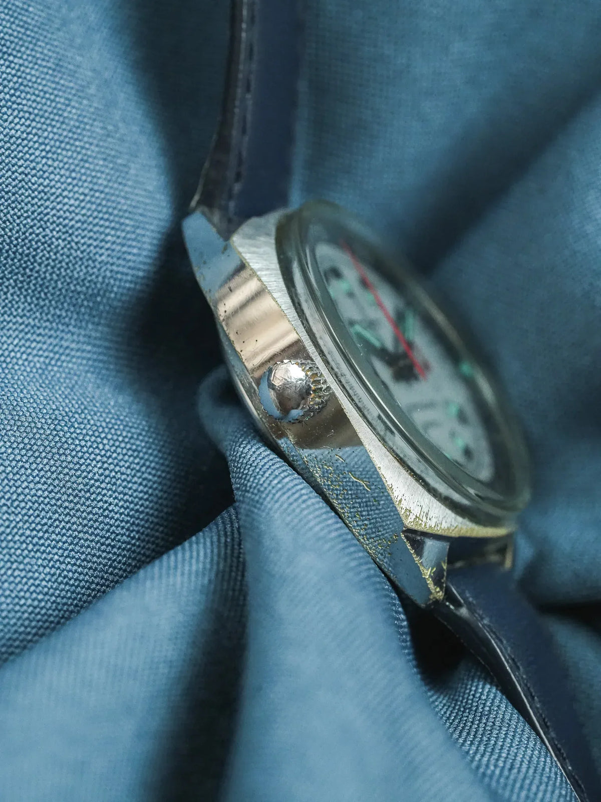 Vintage Omega watch with steel case, black dial, and leather strap on blue fabric
