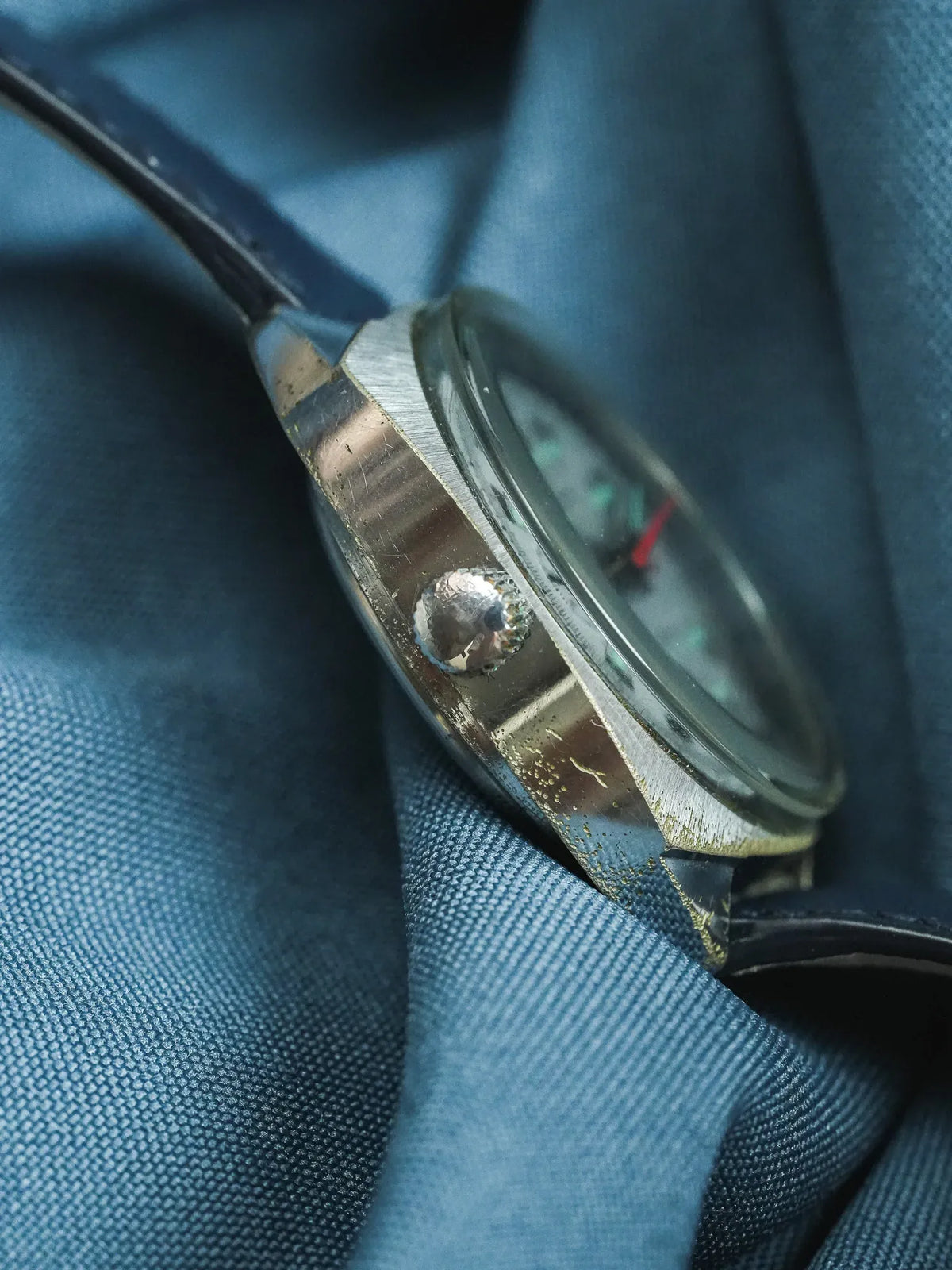 Vintage watch with silver case, black strap, resting on blue fabric