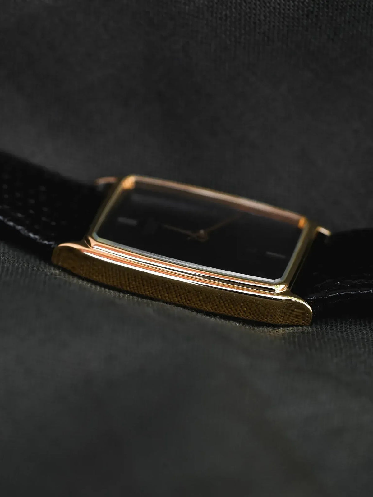 Vintage Cartier watch with gold rectangular case and black dial on dark fabric