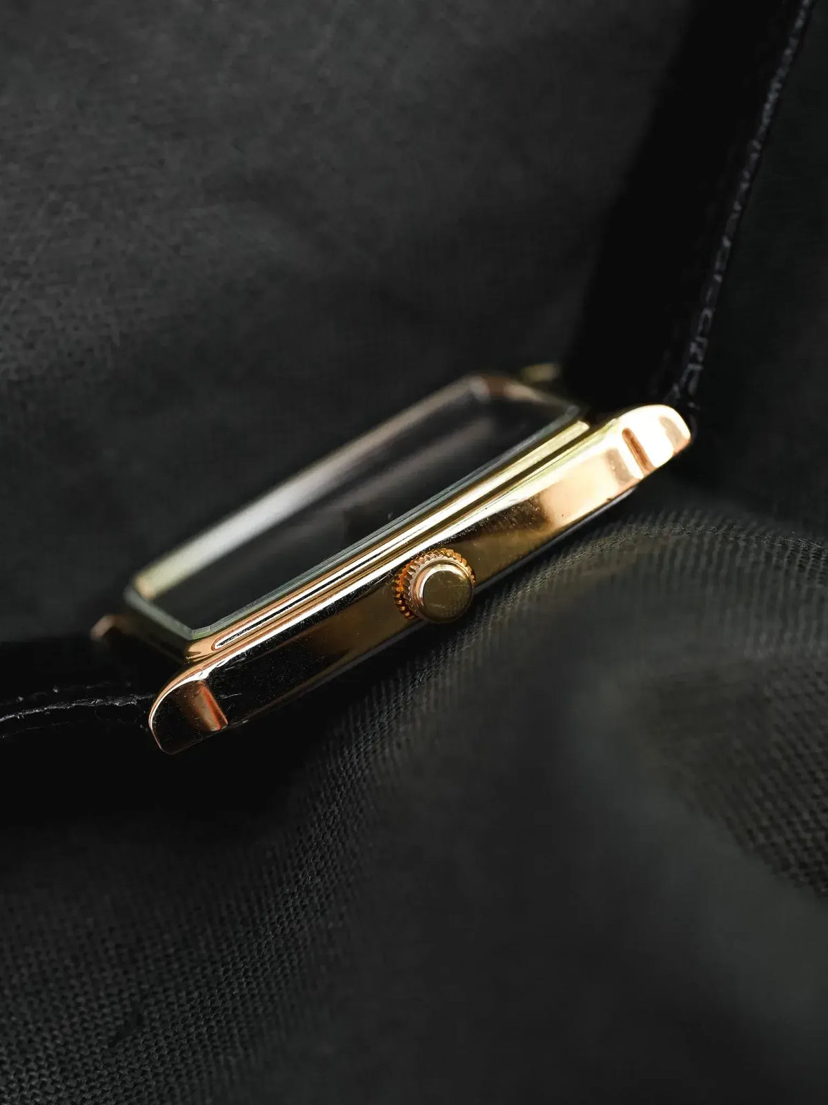 Vintage Cartier Tank watch with gold case and black leather strap on dark fabric