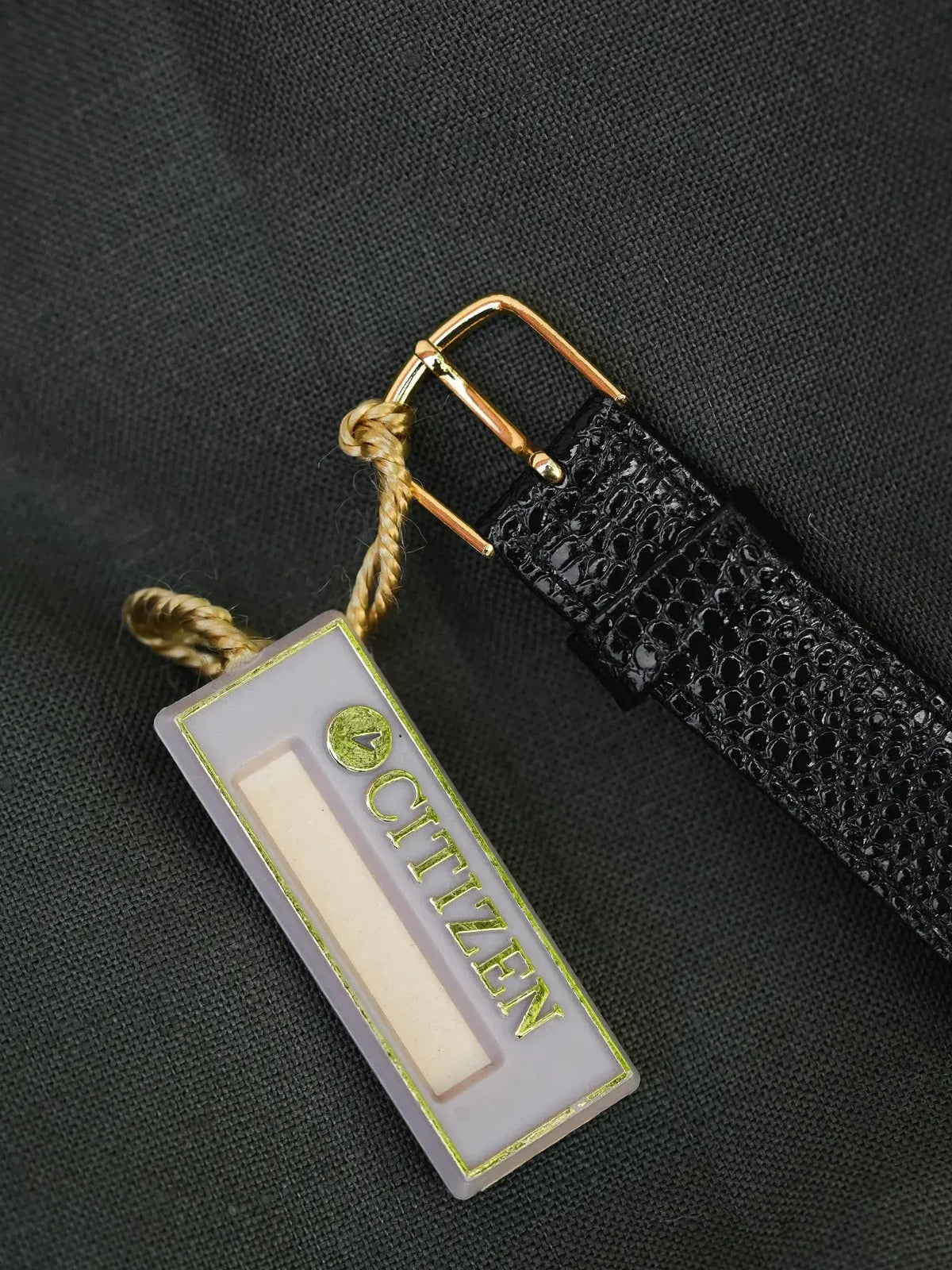 Citizen watch tag with gold lettering on frosted glass, attached to black textured strap