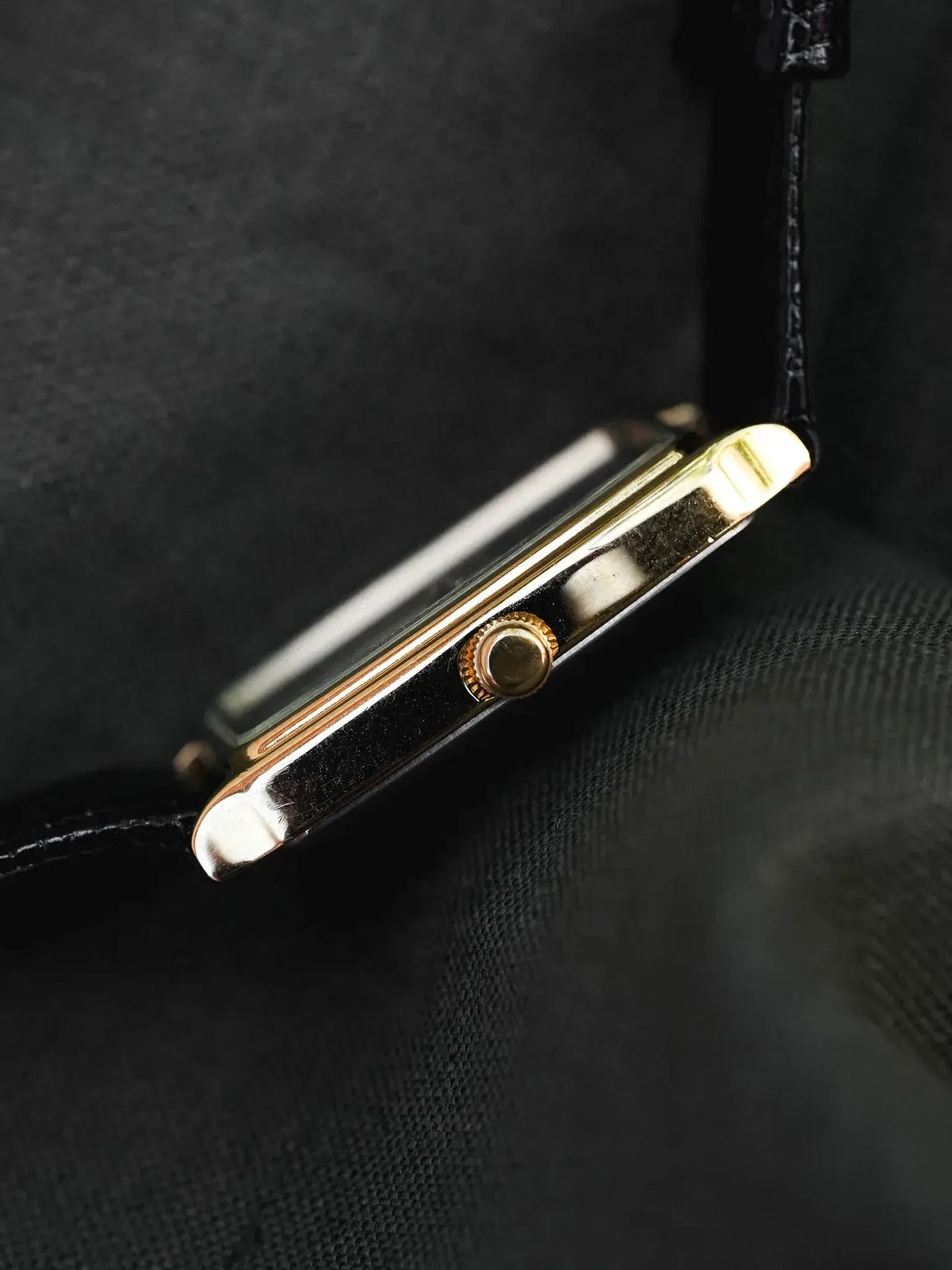 Vintage Cartier Tank watch with gold case and black leather strap on dark fabric