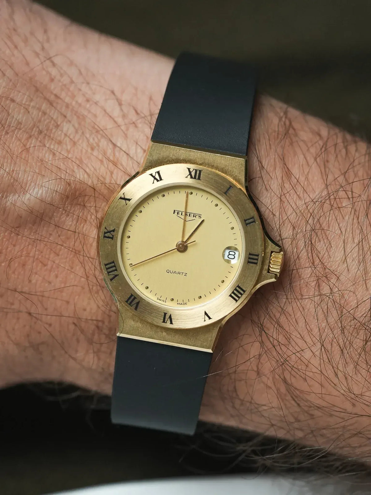 Felser's vintage quartz watch with gold case, cream dial, Roman numerals, black strap on wrist