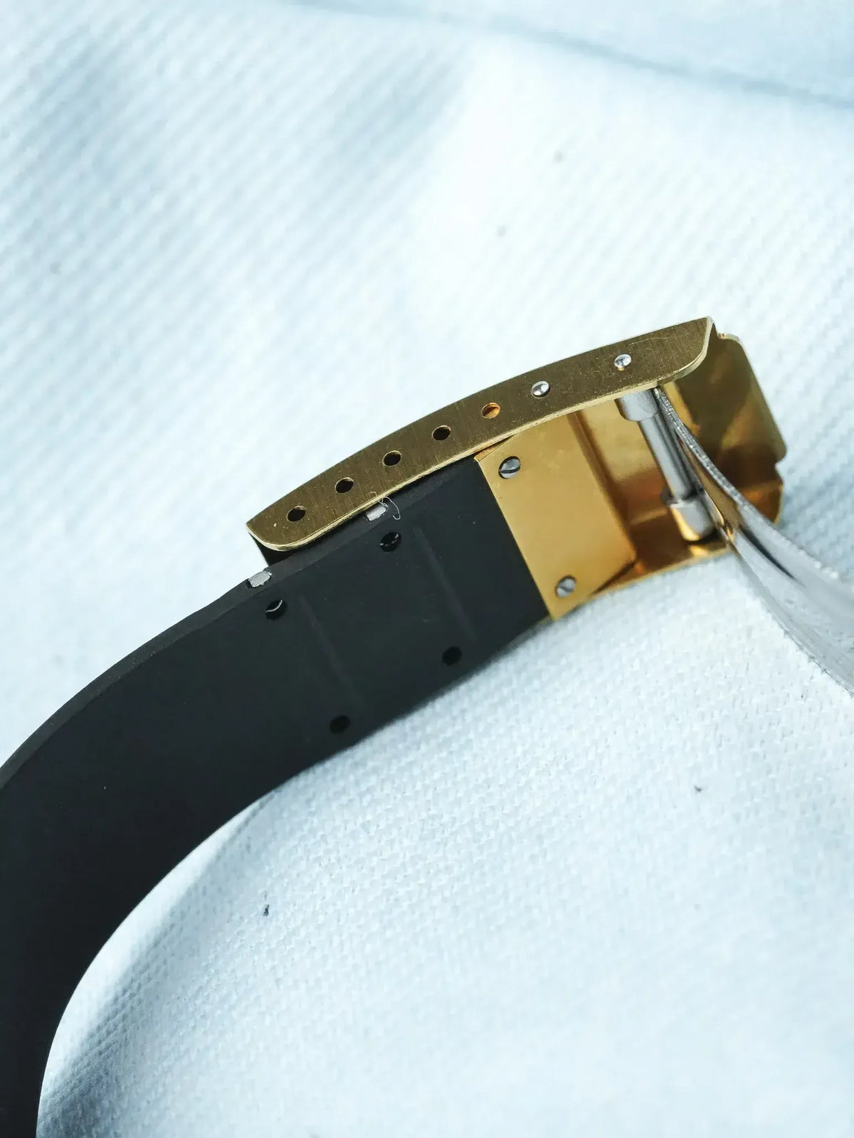 Vintage Cartier watch with gold case and black rubber strap on white fabric