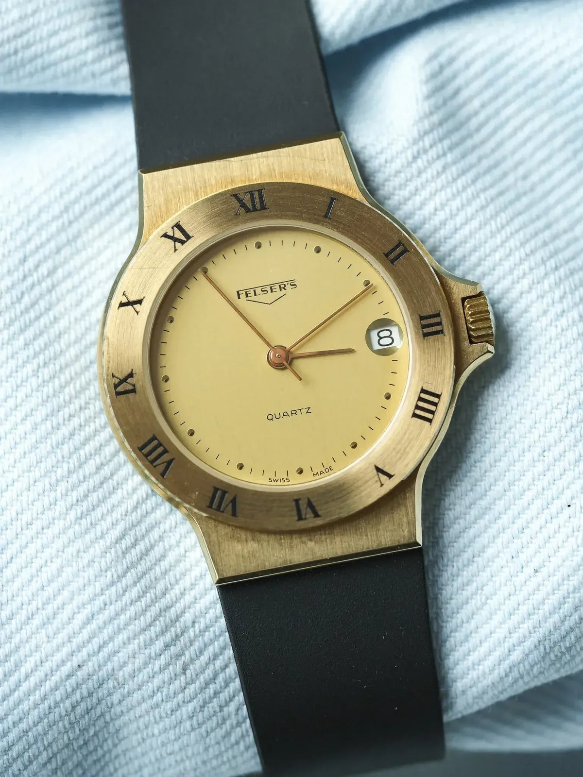 Felser's vintage quartz watch with gold case, cream dial, Roman numerals, black strap on textured fabric