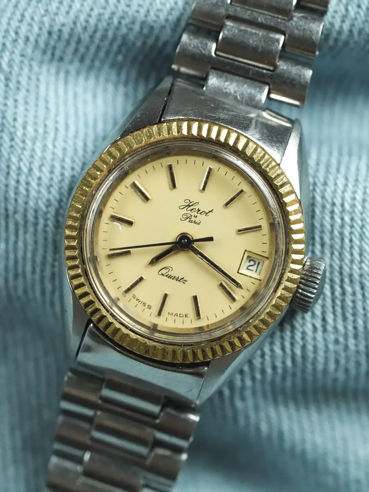 Herot Paris vintage quartz watch with gold bezel, cream dial, and steel bracelet on denim
