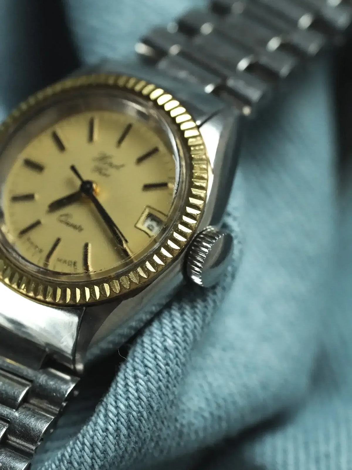 Vintage Omega Seamaster watch with gold bezel, cream dial, and steel bracelet on denim