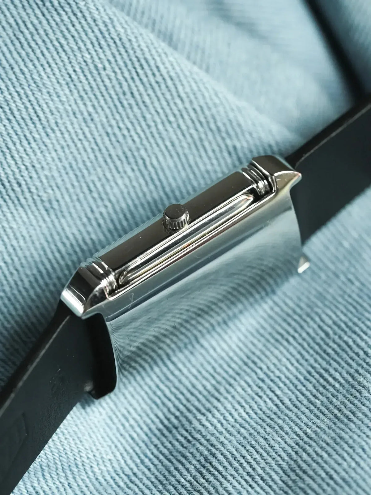 Cartier Tank vintage watch side view, polished steel case, black leather strap on blue fabric